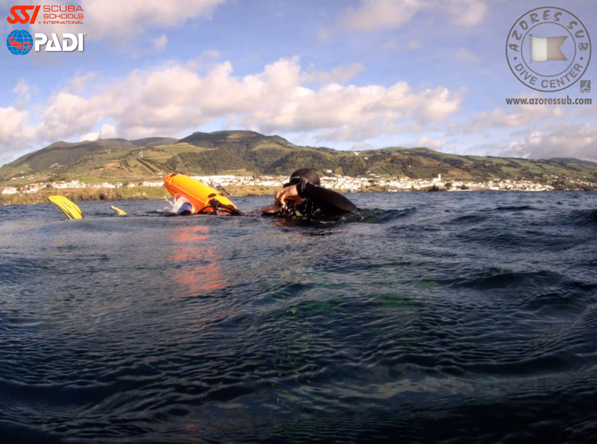Scuba diver practicing PADI Rescue Diver skills with orange float, Azores island town and mountains behind