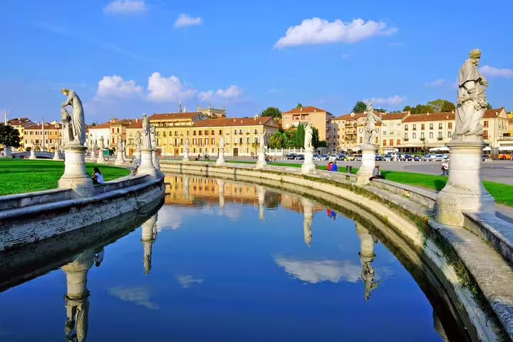 Sunny view of Prato della Valle square in Padua with statue-lined canal and historic palaces on a guided walking tour