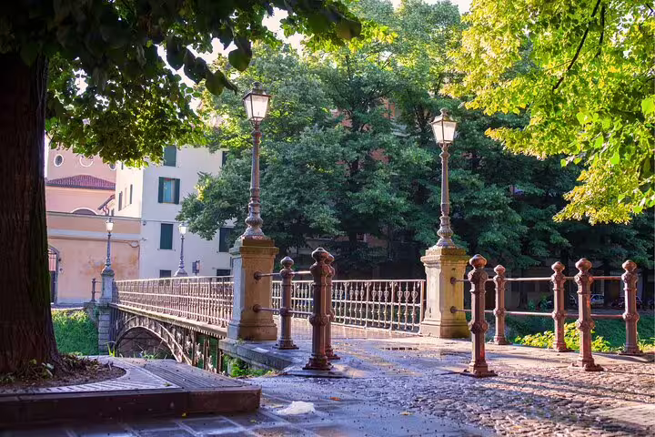 Tree-lined riverside bridge in Padua, Italy, a scenic stop on a self-guided scavenger hunt highlights tour
