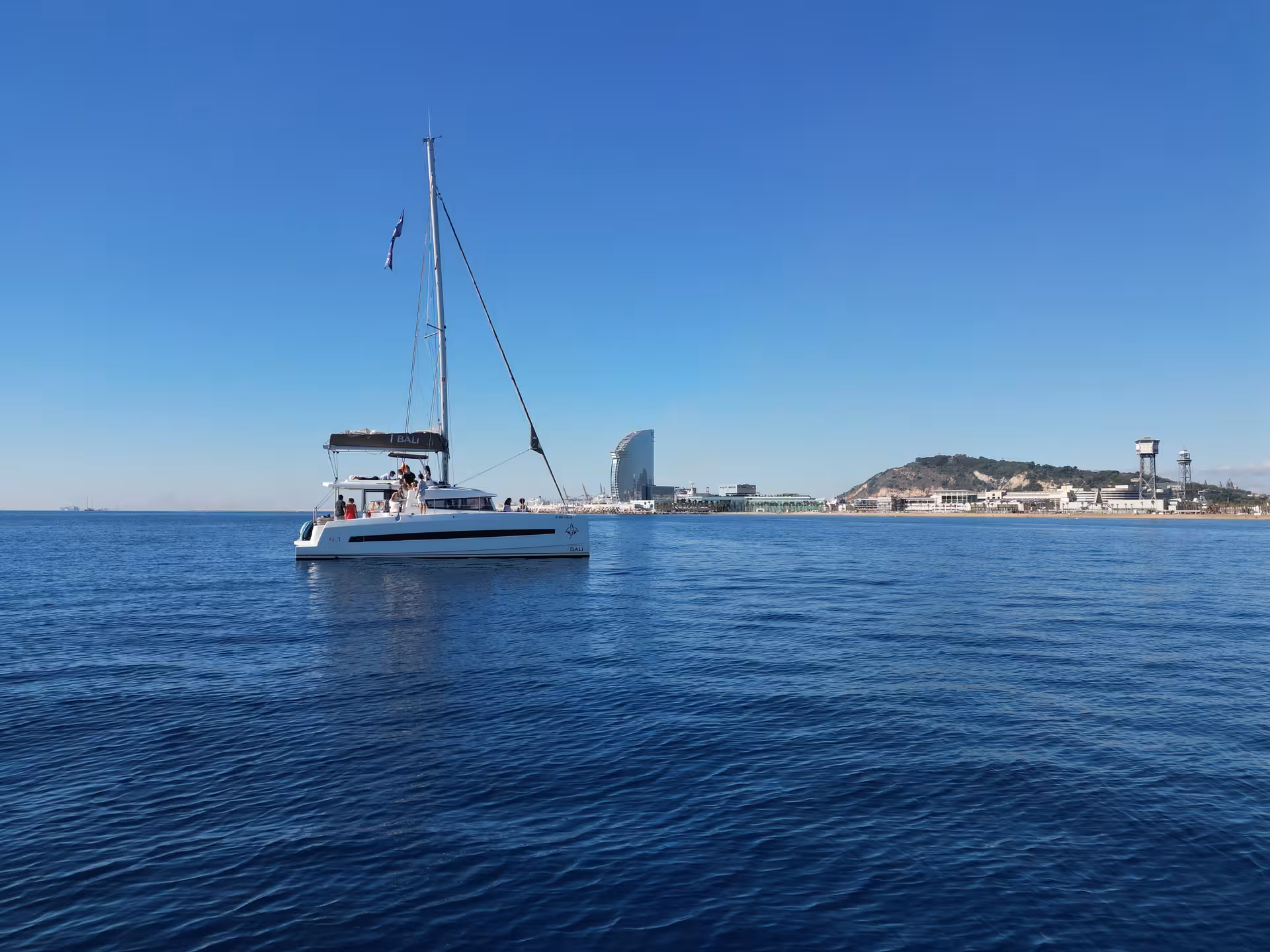 Catamaran sailing near Barcelona coastline, scenic backdrop for a Paella Masterclass with cooking and tasting at sea