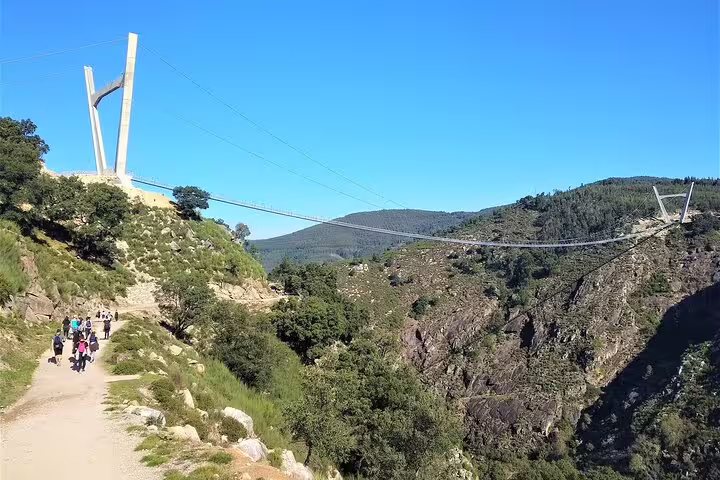 Hikers enjoy scenic views on the Paiva Walkways with the Arouca Suspension Bridge spanning rugged landscapes under a clear blue sky.