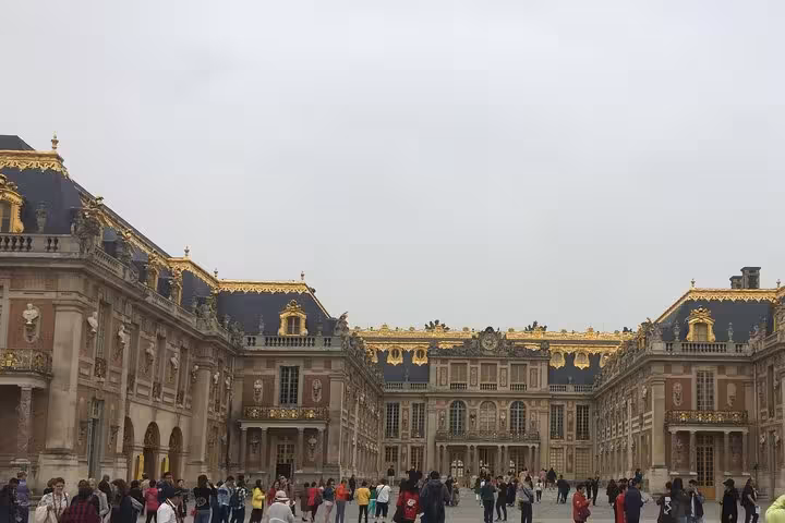 Tourists gathered in the courtyard of the Palace of Versailles with ornate golden facade