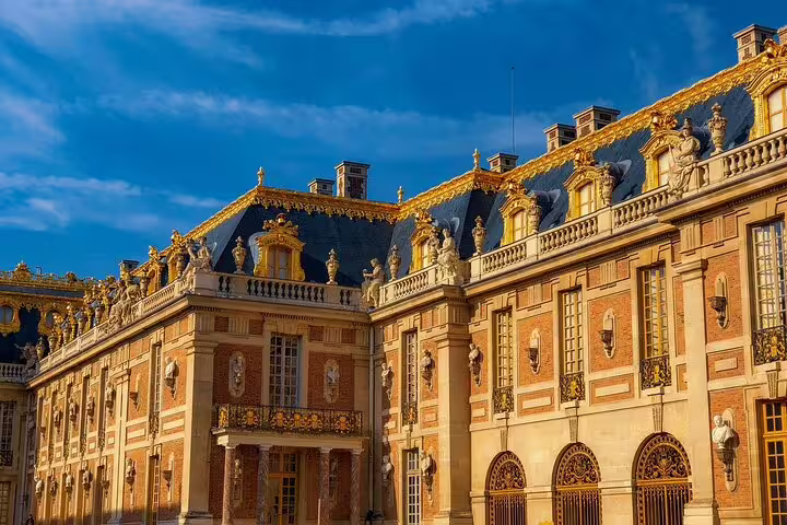 Ornate golden facade of the Palace of Versailles with baroque architecture under blue sky