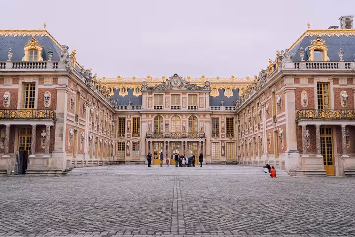 Ornate marble courtyard facade of the Palace of Versailles with gilded decorations and visitors
