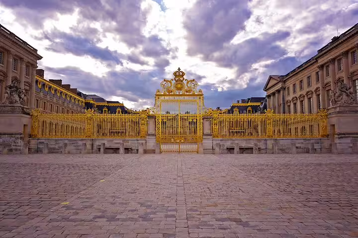 Golden royal gates of the Palace of Versailles with ornate gilded fence and cobblestone courtyard