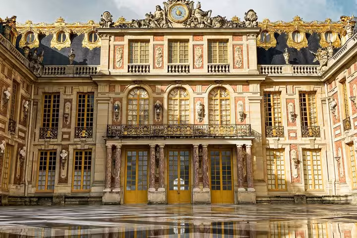 Ornate marble courtyard facade of Palace of Versailles with gilded doors, columns, and baroque sculptures