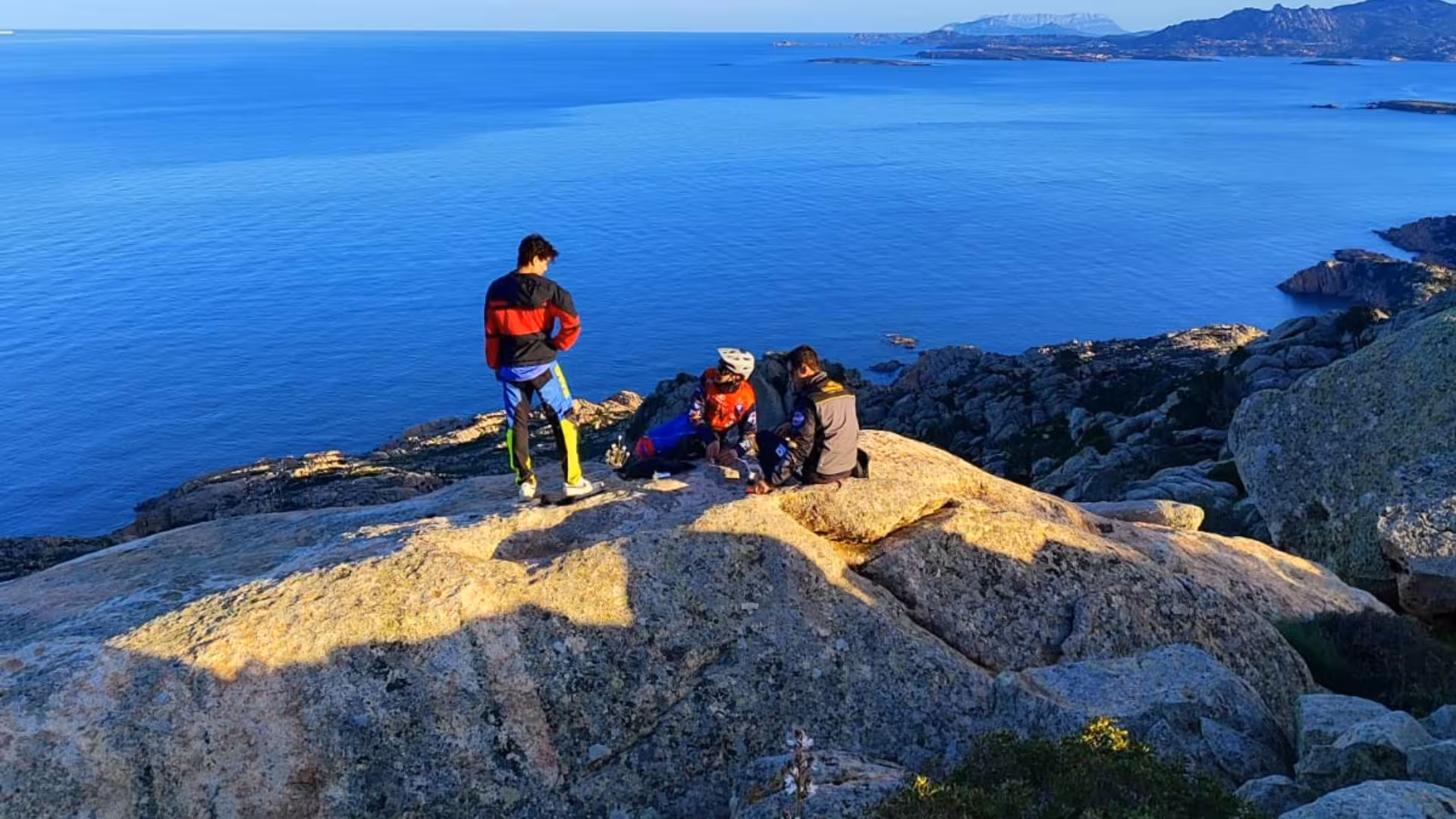 Group of cyclists enjoying a stunning ocean view from a rocky vantage point on the Palau tour to Caprera or La Maddalena.