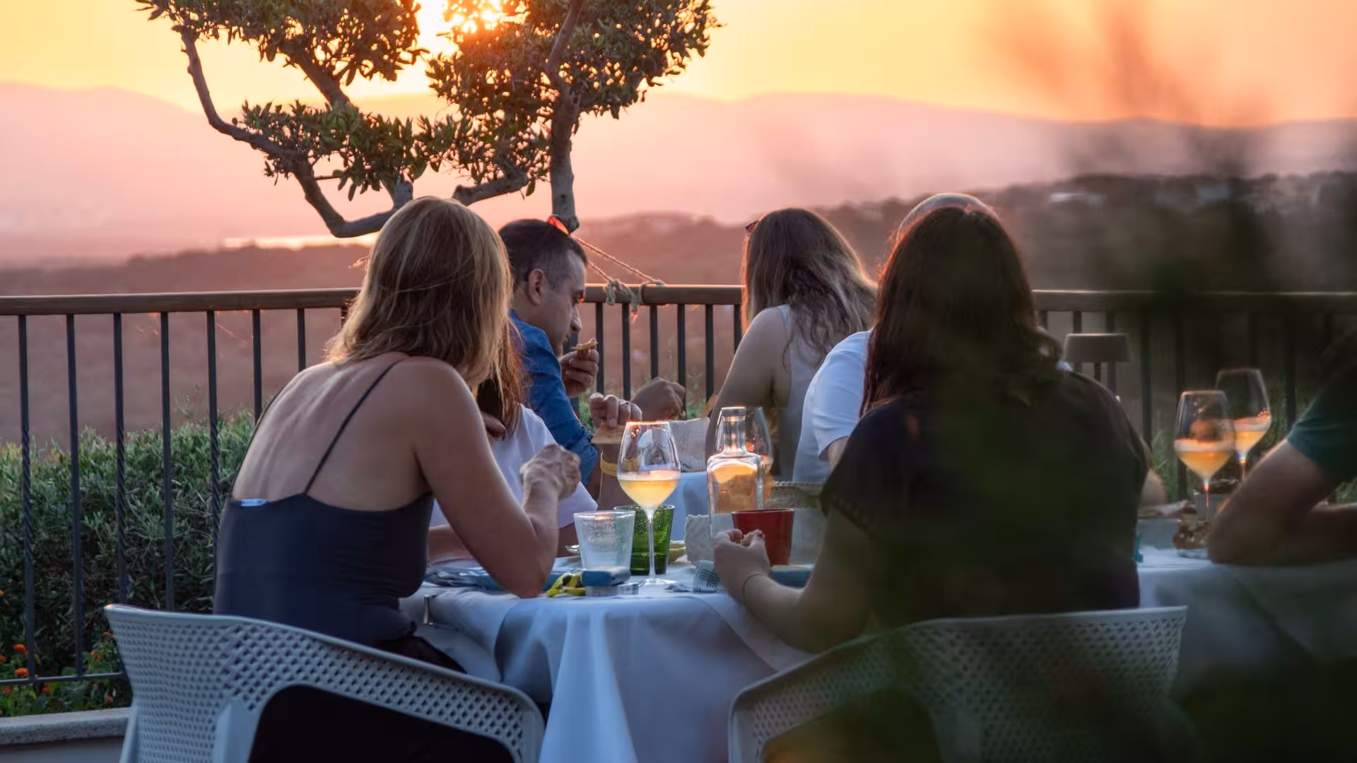 Group savoring wine at a Gallura winery terrace in Palau, overlooking a vibrant sunset view.