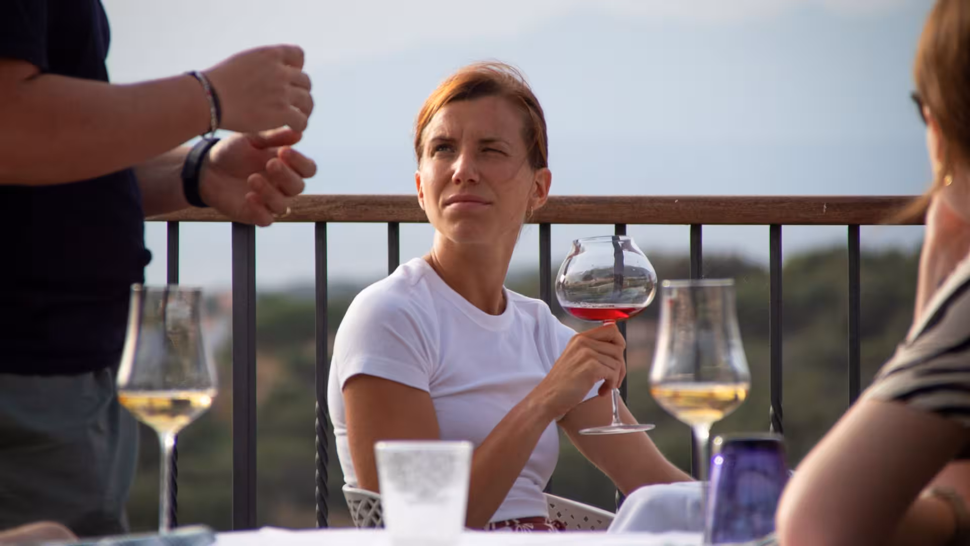 Woman enjoying wine tasting on a sunny terrace at a Gallura winery in Palau, savoring local flavors.