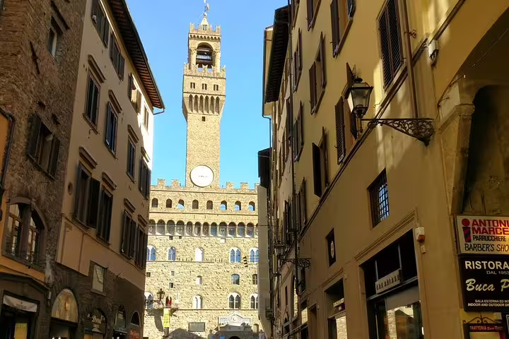 Narrow street in Florence leading to Palazzo Vecchio tower under blue sky