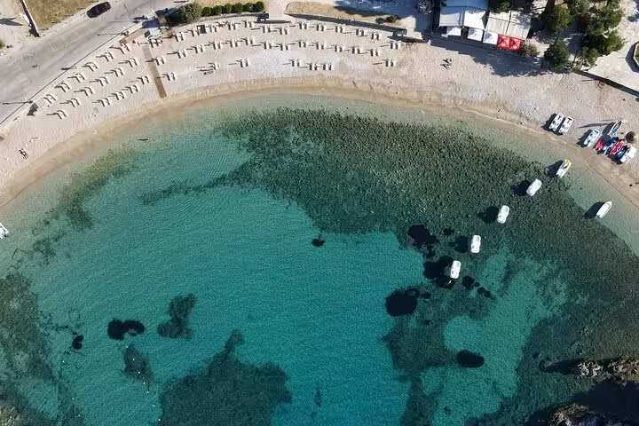 Drone view of Paleokastritsa bay Corfu with clear water, boats and sandy shore on a private beaches tour