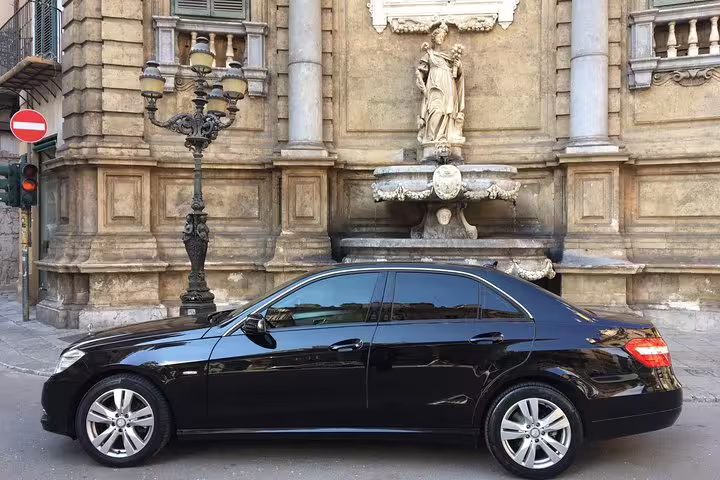 Luxury black sedan parked by historic Palermo landmark, used for private airport transfer to ibis Styles Palermo Cristal