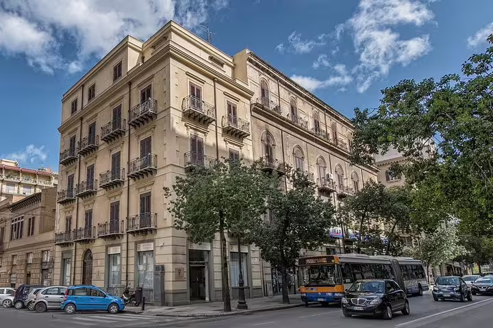 Street view of historic Palermo building with traffic, en route private transfer from airport to Artemisia Palace Hotel