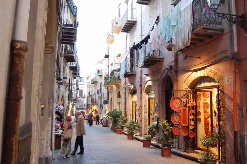Charming historic street in Cefalù with shops, balconies and locals, ideal arrival point after Palermo airport transfer