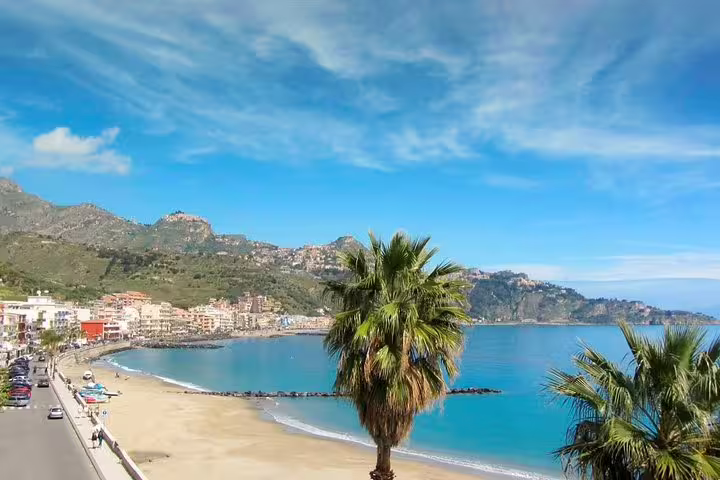Sunny Giardini Naxos beach with palm trees and turquoise sea, destination of private transfer from Palermo Airport