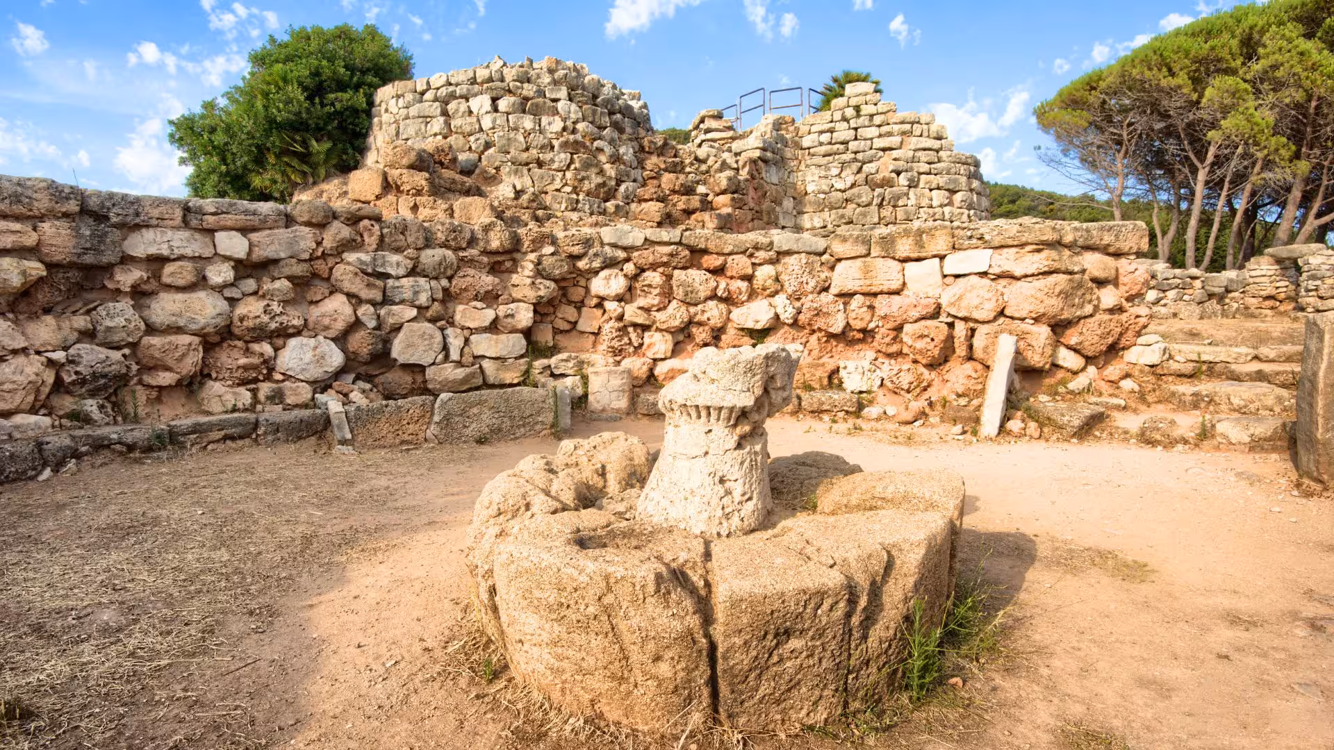 Wide view of Palmavera Nuraghe ruins in Alghero, featuring ancient stone walls and a clear blue sky backdrop.