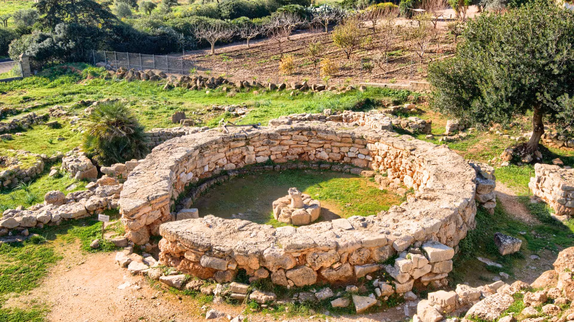 Explore the ancient stone ruins of Palmavera nuraghe surrounded by lush greenery near Alghero, Sardinia.