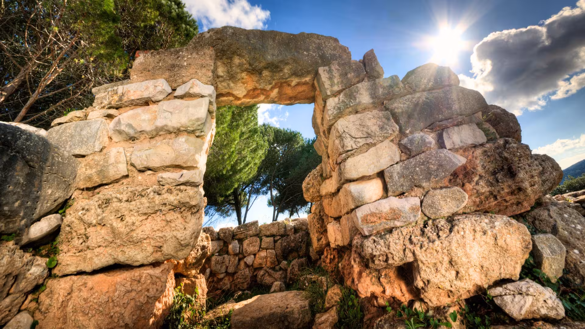 Explore the ancient stone archway of Palmavera Nuraghe in Alghero, illuminated by the sun.