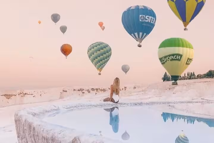 Woman by Pamukkale thermal pool with hot air balloons overhead at sunrise, Turkey Pamukkale balloon flight