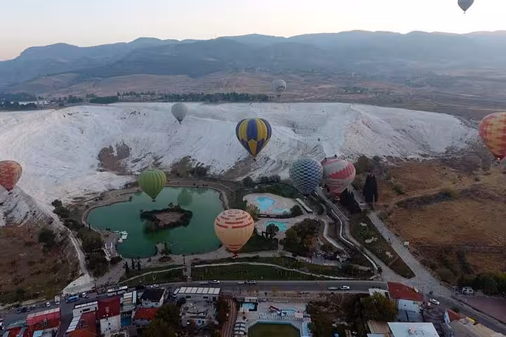 Pamukkale balloon tour aerial view of travertine cliffs, green lake and multiple balloons at sunrise