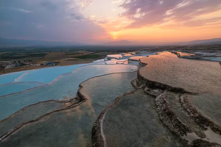 Breathtaking sunset over Pamukkale's terraced pools, with shimmering waters reflecting the vibrant evening sky.