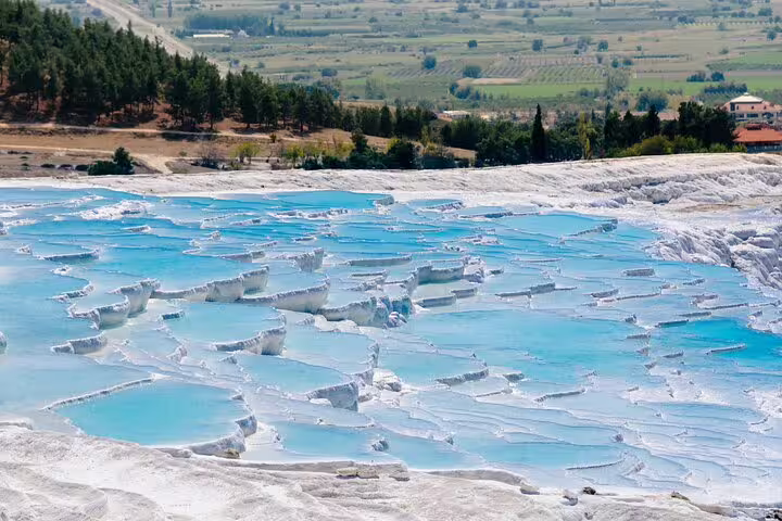 Stunning view of Pamukkale's turquoise thermal terraces surrounded by lush green landscape, ideal for a private tour.