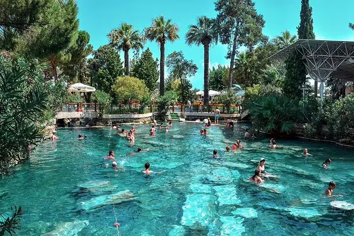 Visitors enjoy the thermal waters of Pamukkale's Antique Pool surrounded by lush greenery on a tour from Izmir.