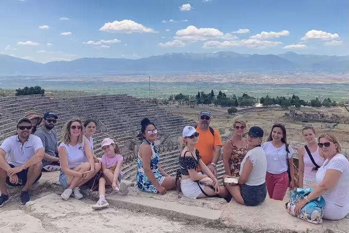 A tour group seated on ancient amphitheater steps with panoramic views of Pamukkale's landscape.