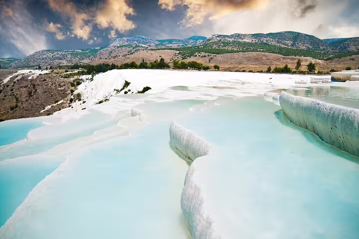 Stunning Pamukkale travertine terraces with turquoise waters under a dramatic sky on a guided tour from Istanbul.