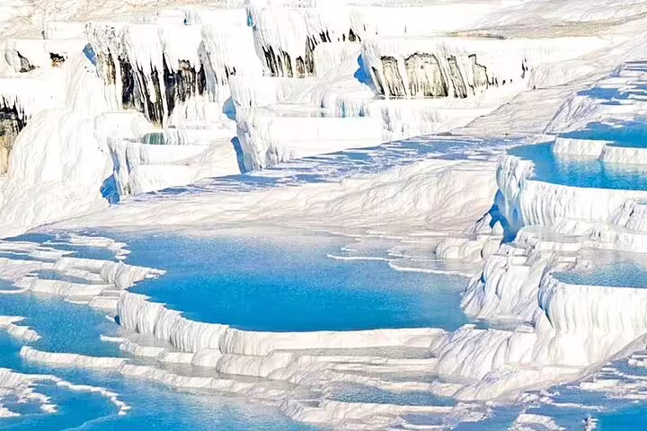 Bright white travertine terraces with turquoise pools in Pamukkale, perfect for a small group tour from Izmir.