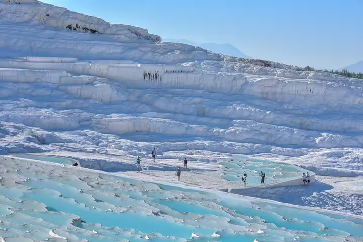 Visitors explore Pamukkale's stunning white travertine terraces and turquoise thermal pools, a must-see on a day tour from Istanbul.