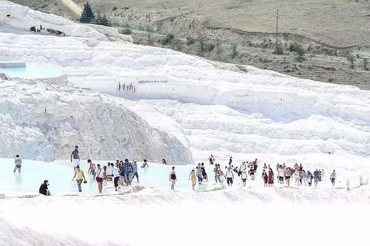 Visitors enjoying the unique experience of Pamukkale's cascading white travertine terraces on a sunny day.