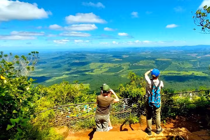 Tourists capturing breathtaking panoramic views of vast green landscapes from a scenic lookout point on a sunny day.
