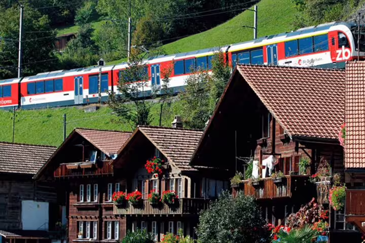 Panoramic Swiss train journey passing traditional wooden chalets adorned with flowers in a lush green valley.