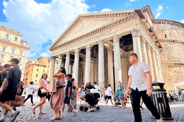 Visitors stroll in front of Rome's iconic Pantheon under a blue sky, highlighting its architectural magnificence.