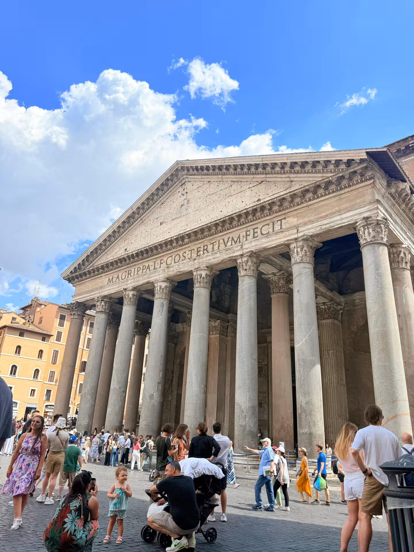Tourists gather outside the historic Pantheon in Rome under a clear blue sky, highlighting its grand Corinthian columns.