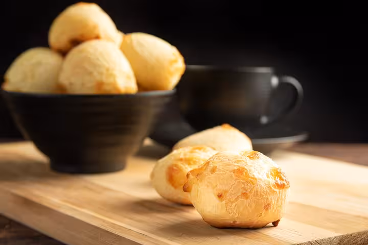 A close-up of freshly baked pão de queijo on a wooden board, a staple in Bahian cooking classes in Salvador.