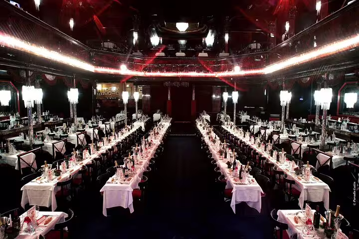 Paradis Latin cabaret dining hall in Paris with long banquet tables set for dinner and a stage