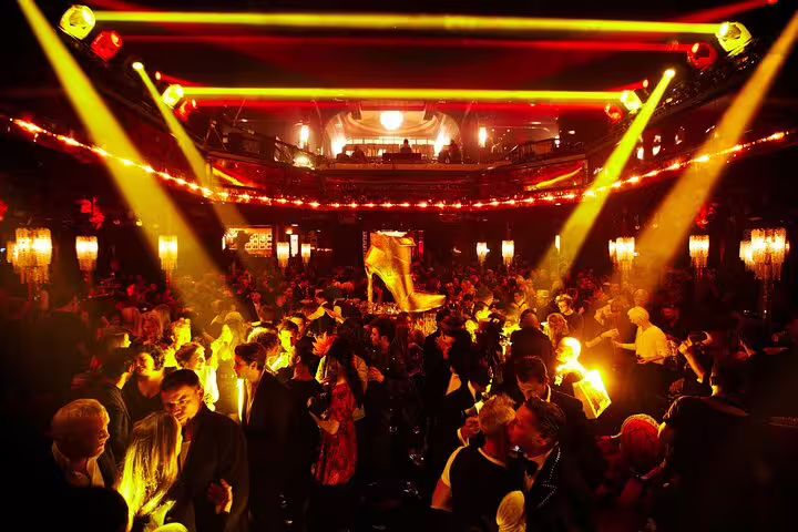 Crowded Paradis Latin cabaret in Paris with yellow and red stage lights illuminating the dance floor