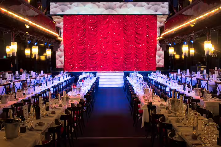 Elegant dinner hall at Paradis Latin cabaret Paris with red stage curtain and long dining tables set for guests