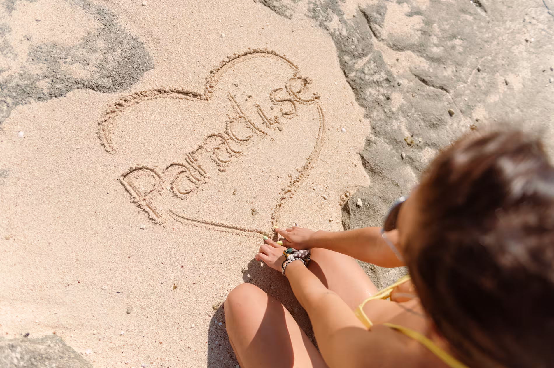Woman writing Paradise in a heart shape on sandy beach at Giftun Island