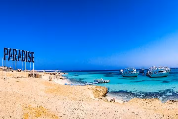 Paradise Island beach sign with boats in crystal-clear Red Sea, Paradise Island from Hurghada snorkeling tour