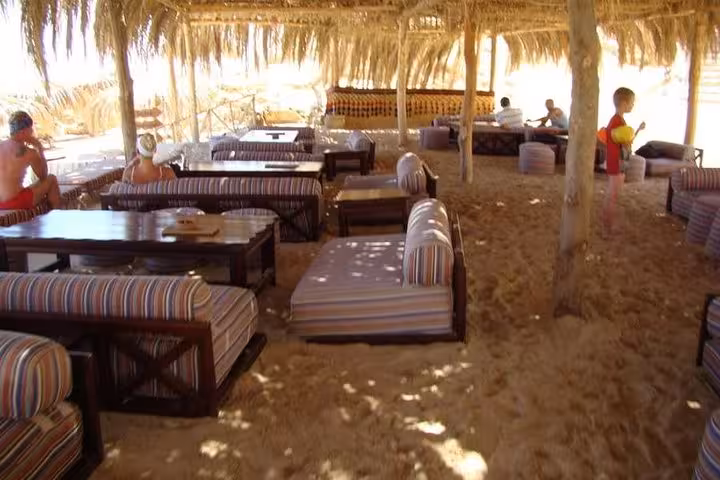 Shaded beach lounge seating on Paradise Island Hurghada tour, with cushioned sofas on sand under palm thatch