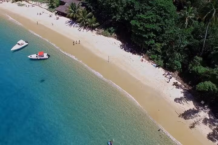 Aerial view of a pristine sandy beach with speedboats anchored near lush green foliage on a Paradise Island tour.