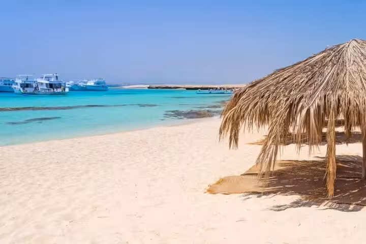 Paradise Island beach from Hurghada VIP boat trip, turquoise Red Sea lagoon, moored yachts and palm shade hut