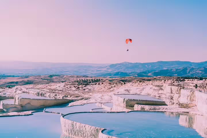 Paraglider soaring above Pamukkale's famous travertine terraces, capturing the breathtaking views on a day tour.