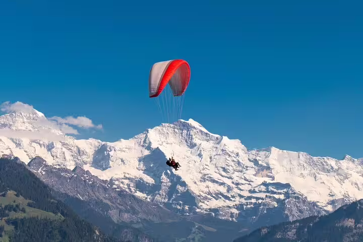 Paraglider soaring over snow-capped Swiss Alps, showcasing adventure on the Blausee Lake and Interlaken tour.
