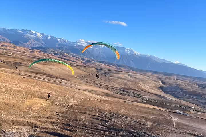 Paragliders soaring over the stunning Agafay Desert landscape with Atlas Mountains in the background.