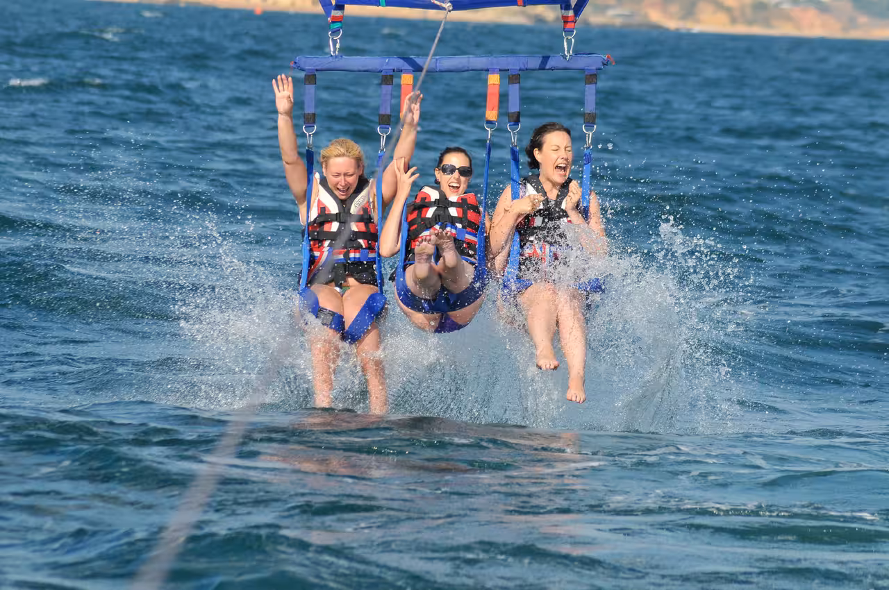 Three excited women in life jackets splashing into the ocean during a thrilling parasailing adventure in Albufeira Algarve