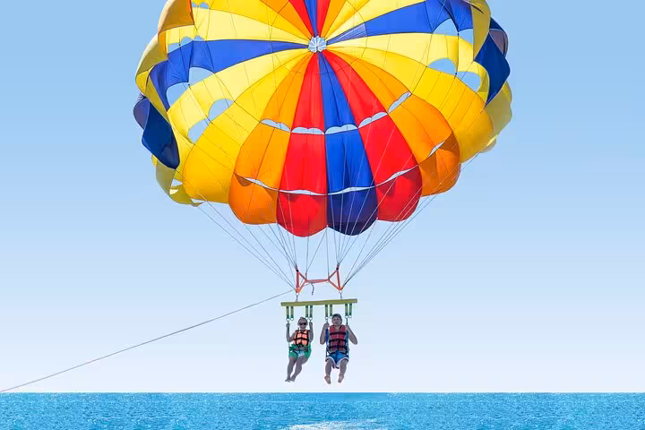 Two tourists parasailing above the Red Sea in Hurghada, colorful canopy and clear blue horizon